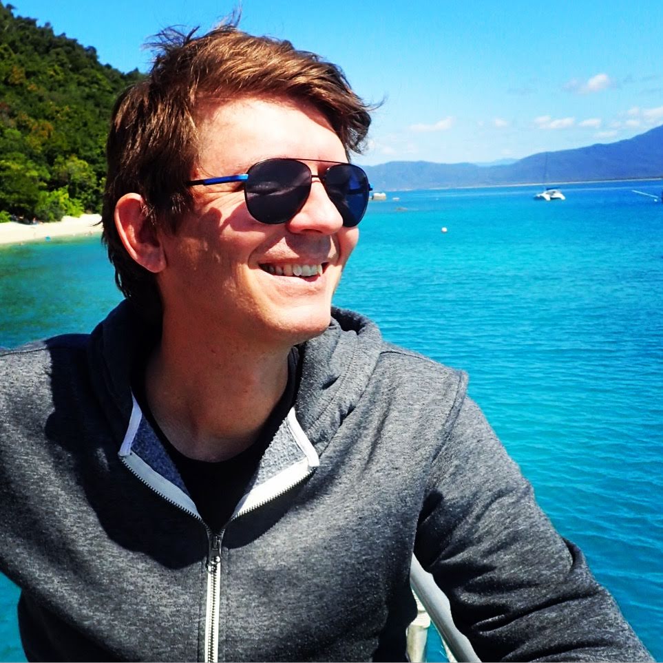 James smiling in a grey top with sun glasses